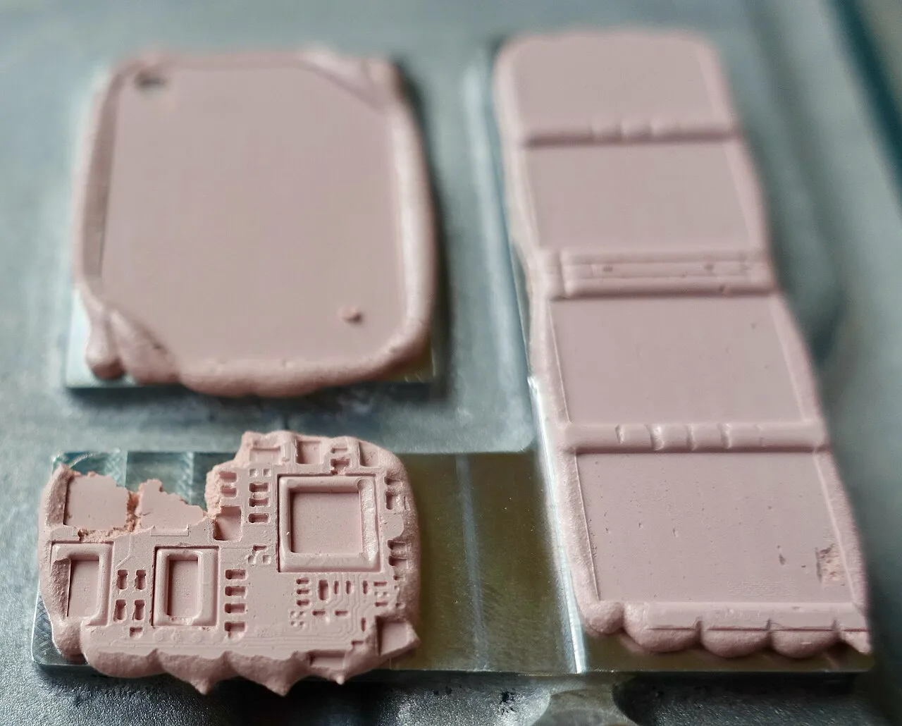 Pink compressible thermal interface material with electronic component outlines pressed into its surface, lifted from a cooling plate
