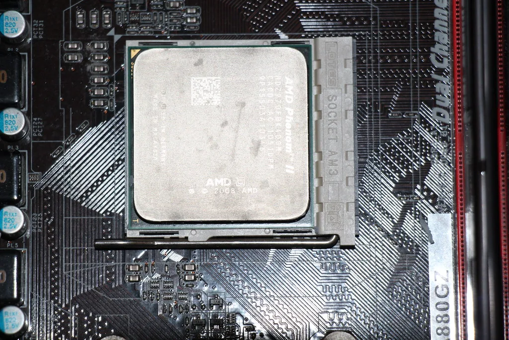 An AMD Phenom II processor seated in an AM3 motherboard socket, its heat spreader covered in a dull film of old gray thermal paste